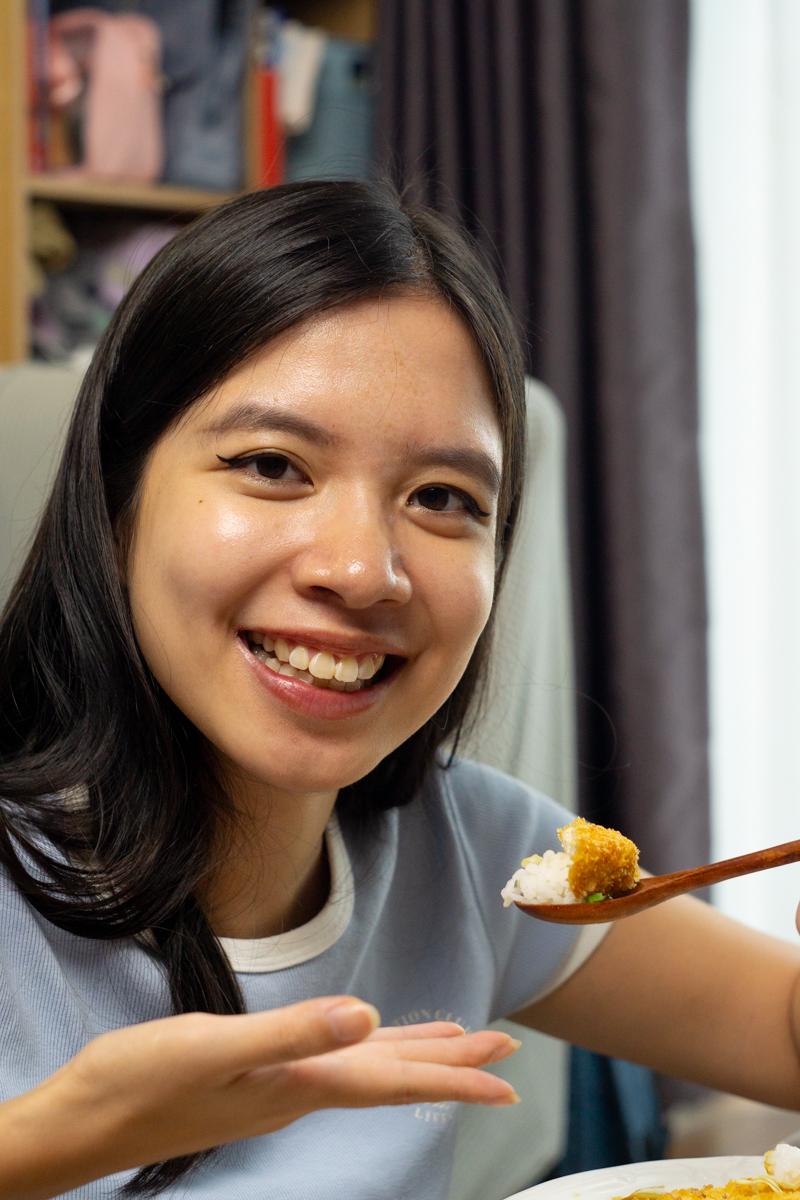 a person smiling while showing a piece of tofu katsu curry