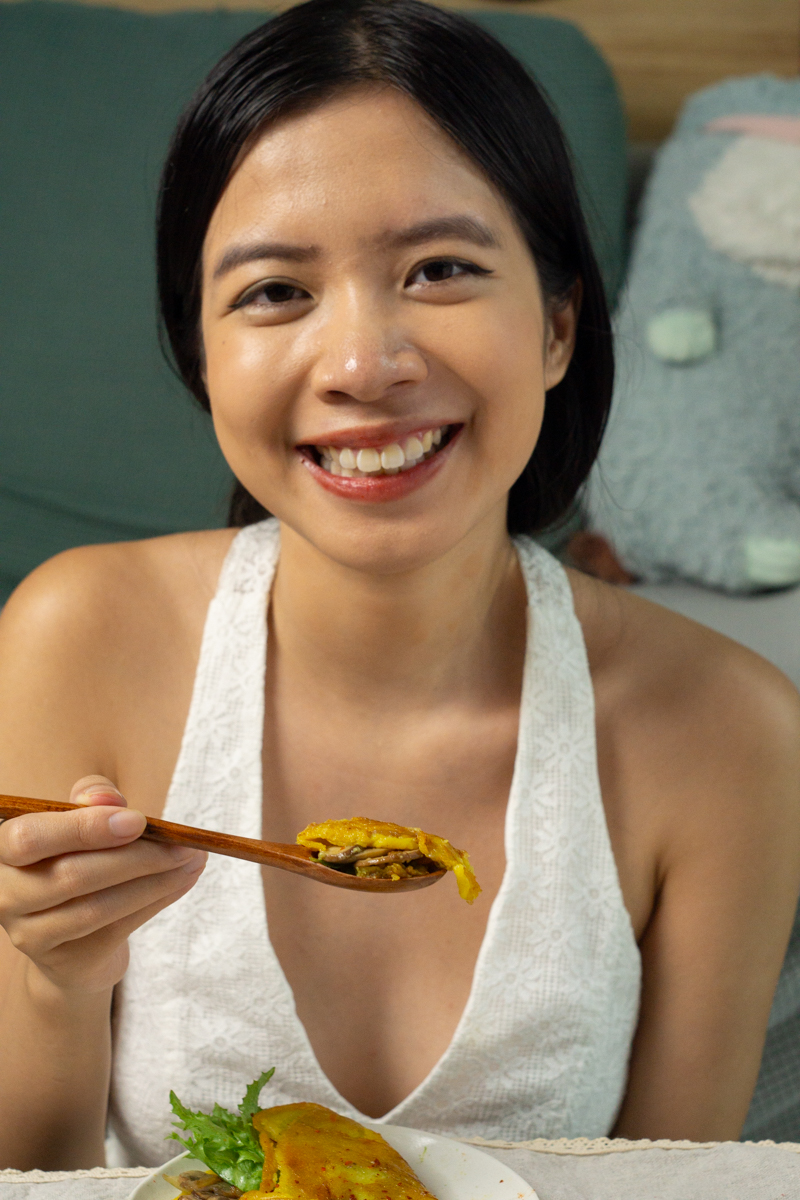 A person smiling while holding a spoon-full of vegan mung bean egg