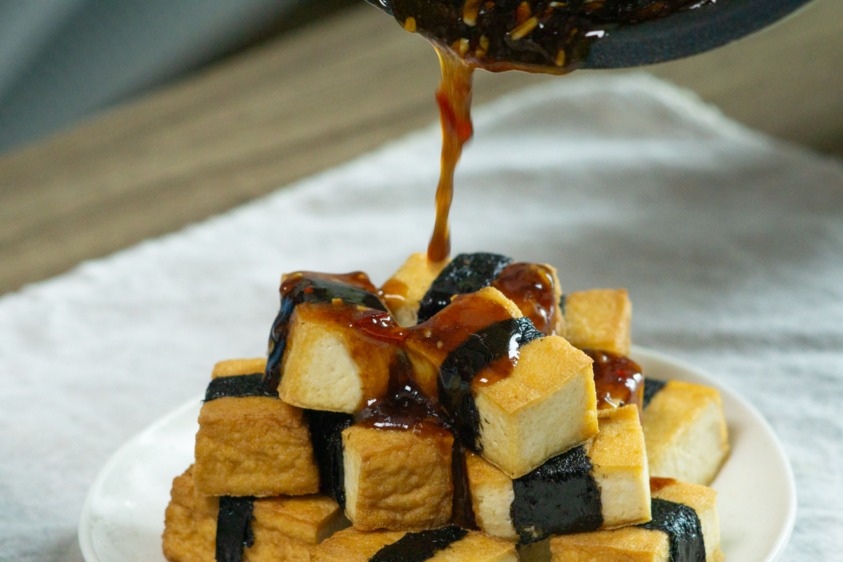 pouring the sauce over the crispy tofu pieces