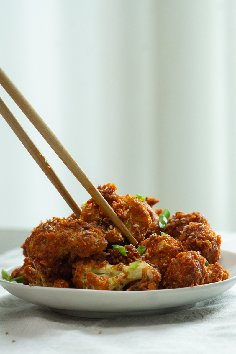 a chopstick picking up a piece of gochujang cauliflower