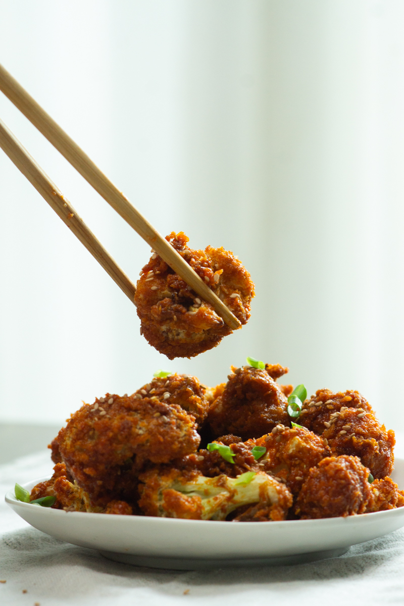 picking up a piece of gochujang cauliflower with chopsticks
